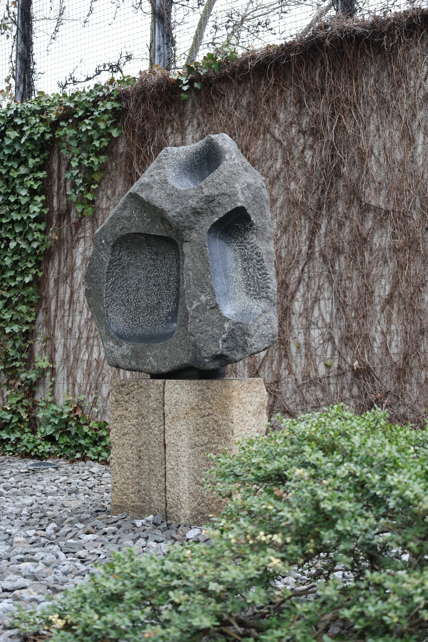 Stone sculpture on pedestal against ivy wall